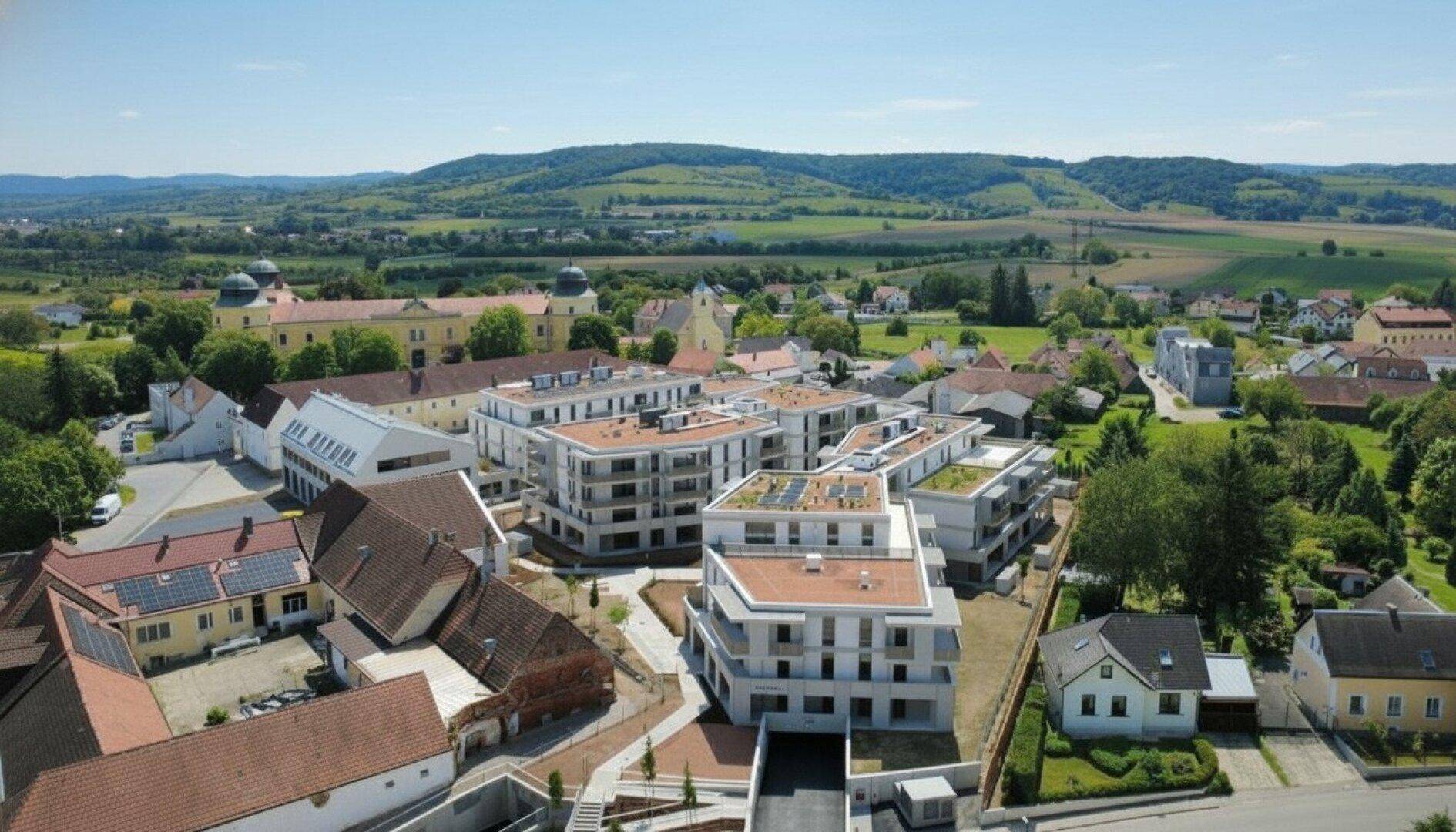 Weitläufige Luftaufnahme der Wohnanlage in einer malerischen Landschaft mit historischen Gebäuden.