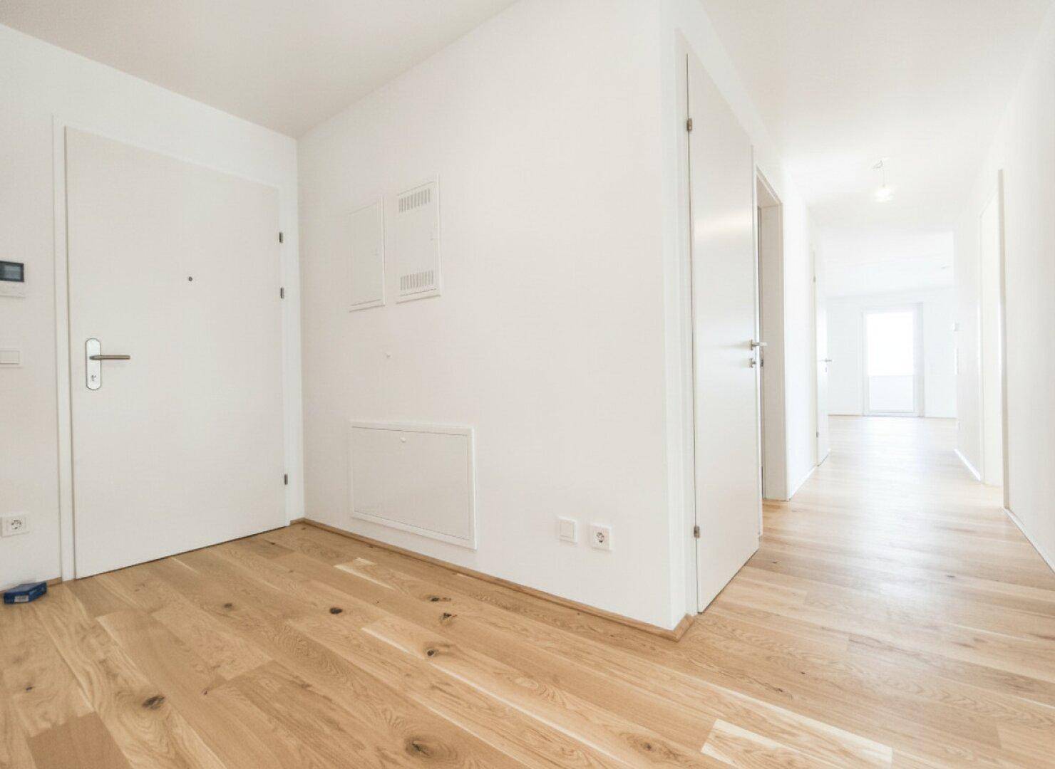 Heller Flur mit Eichenparkettboden, weißen Wänden und Zugang zu verschiedenen Räumen der Wohnung.