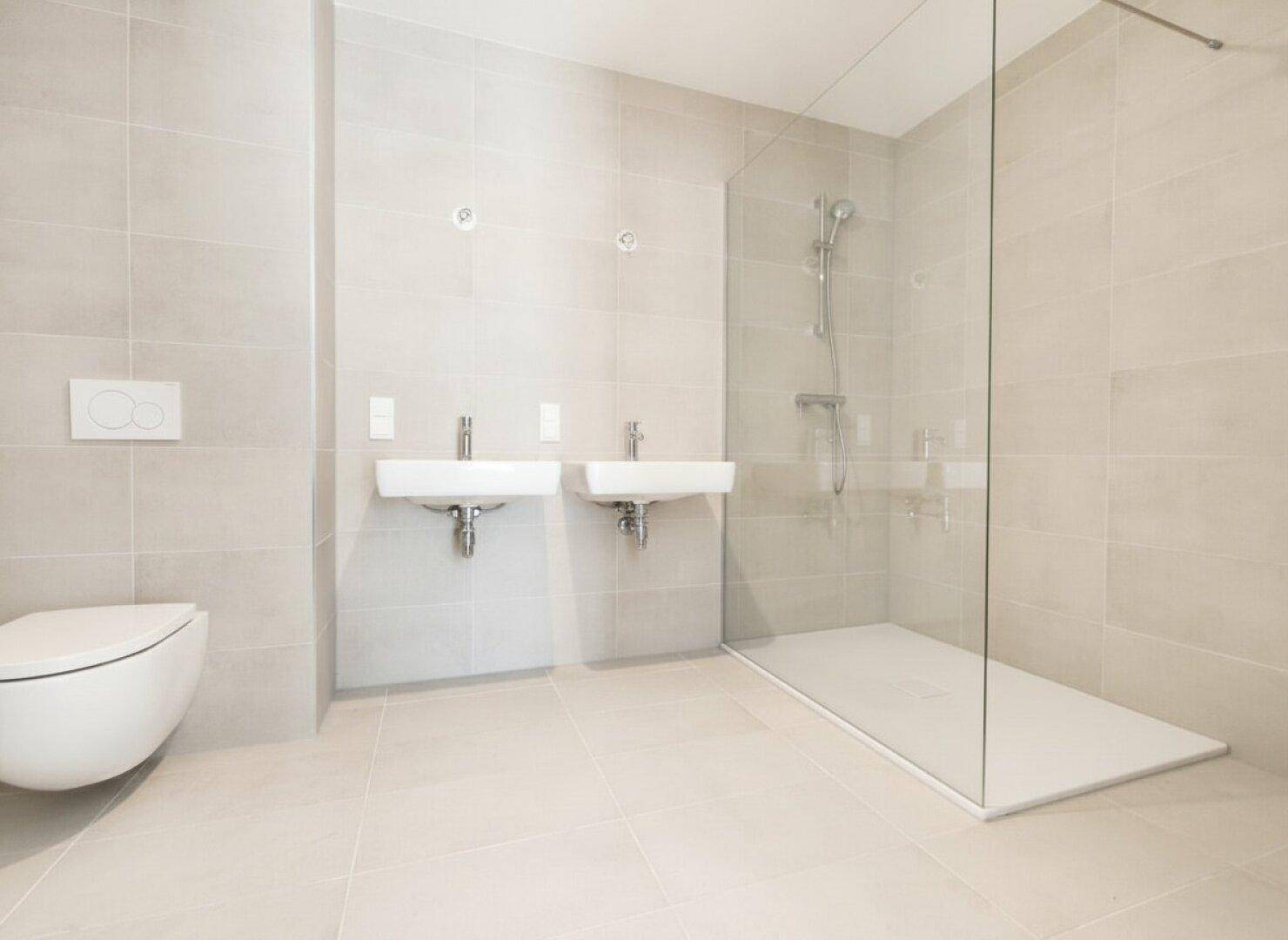 Modernes Badezimmer mit doppelten Waschbecken, bodengleicher Dusche und Wand-WC in hellen Fliesen.
