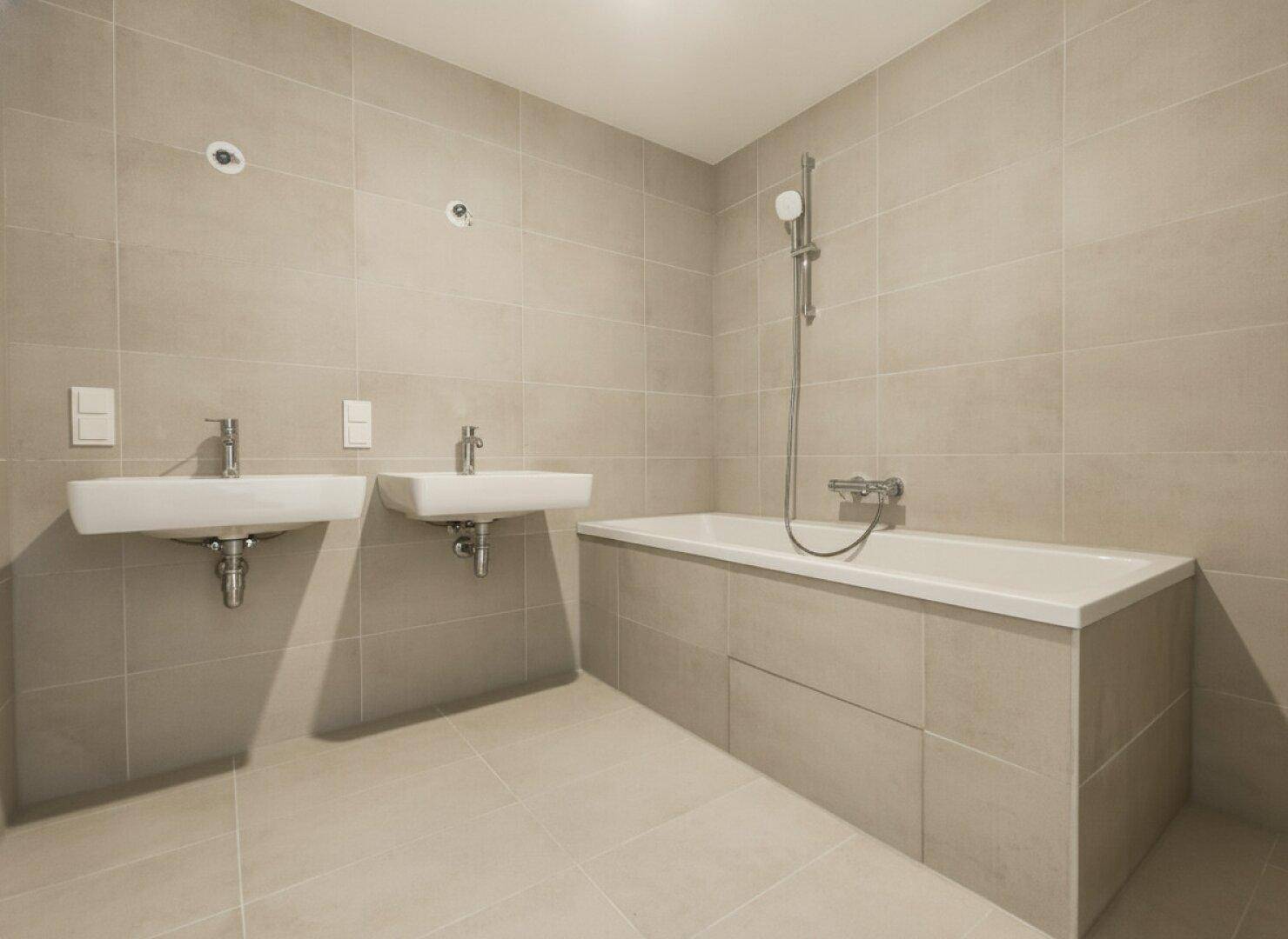 Zeitgemäßes Badezimmer mit Badewanne, zwei Waschbecken und hellen Fliesen an Wänden und Boden.