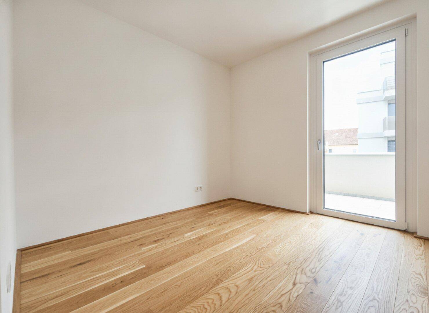Ruhiges Zimmer mit hellem Parkett und Zugang zu einem Außenbereich, perfekt für individuelle Nutzung.
