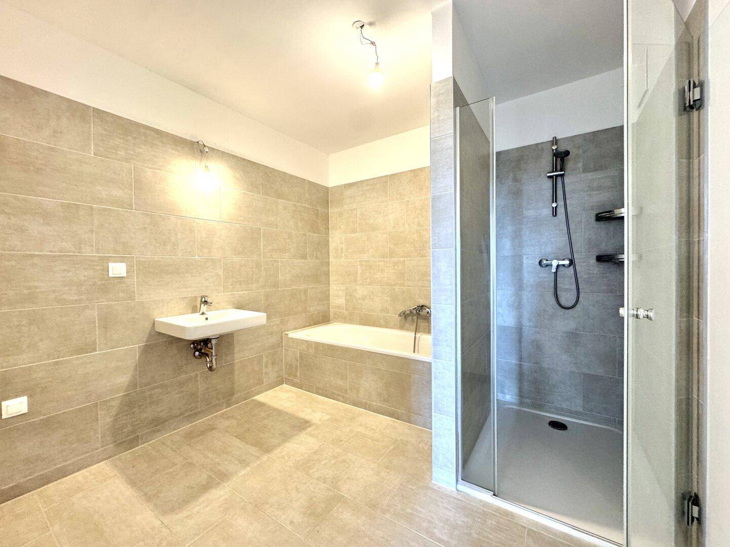 Modernes Badezimmer mit grauen Fliesen, Badewanne und einer geräumigen begehbaren Dusche.
