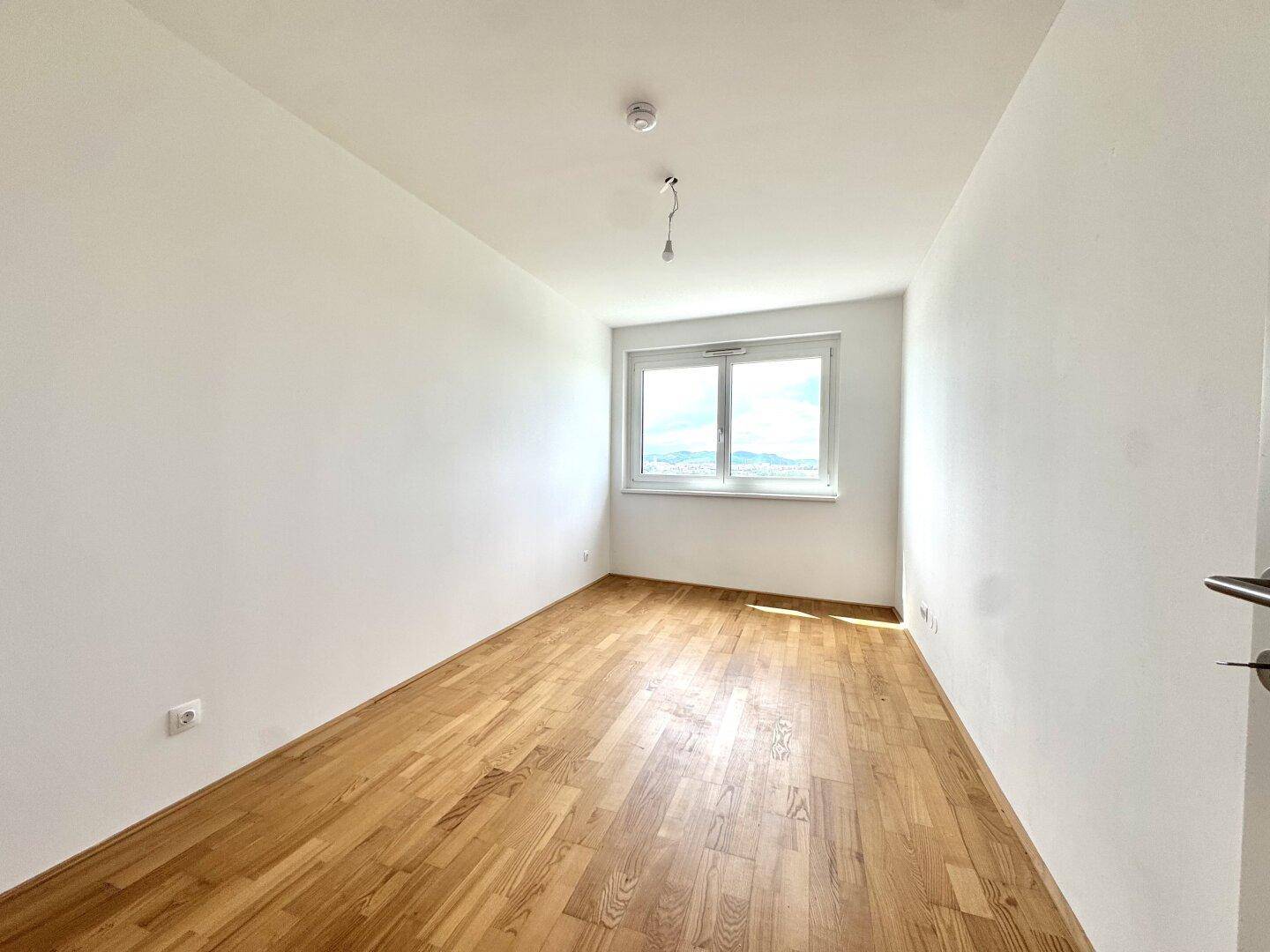 Ruhiges Schlafzimmer mit hellem Parkettboden und großem Fenster für viel Tageslicht.
