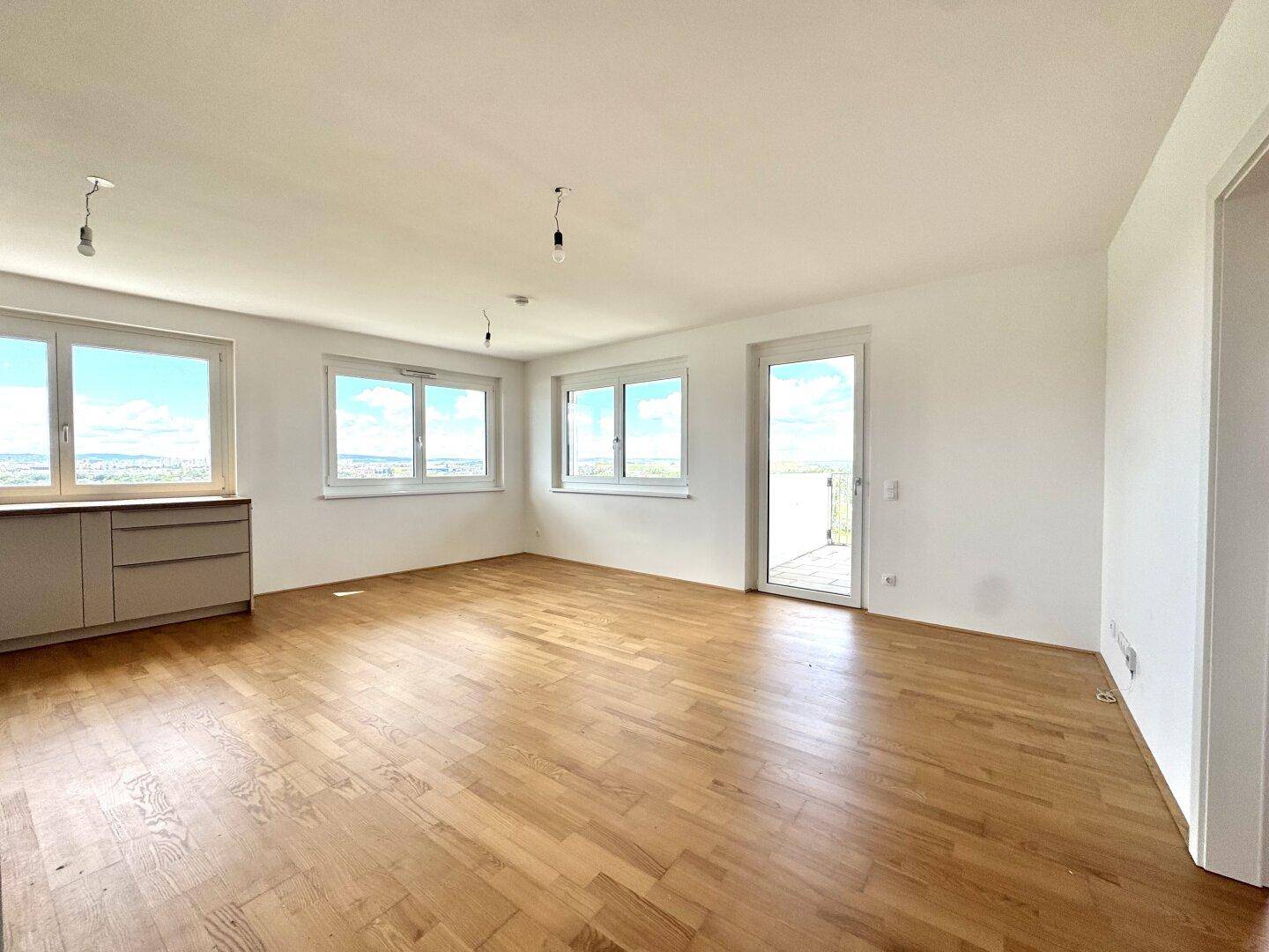 Geräumiges Wohnzimmer mit Parkettboden, großen Fenstern und Zugang zum Balkon.