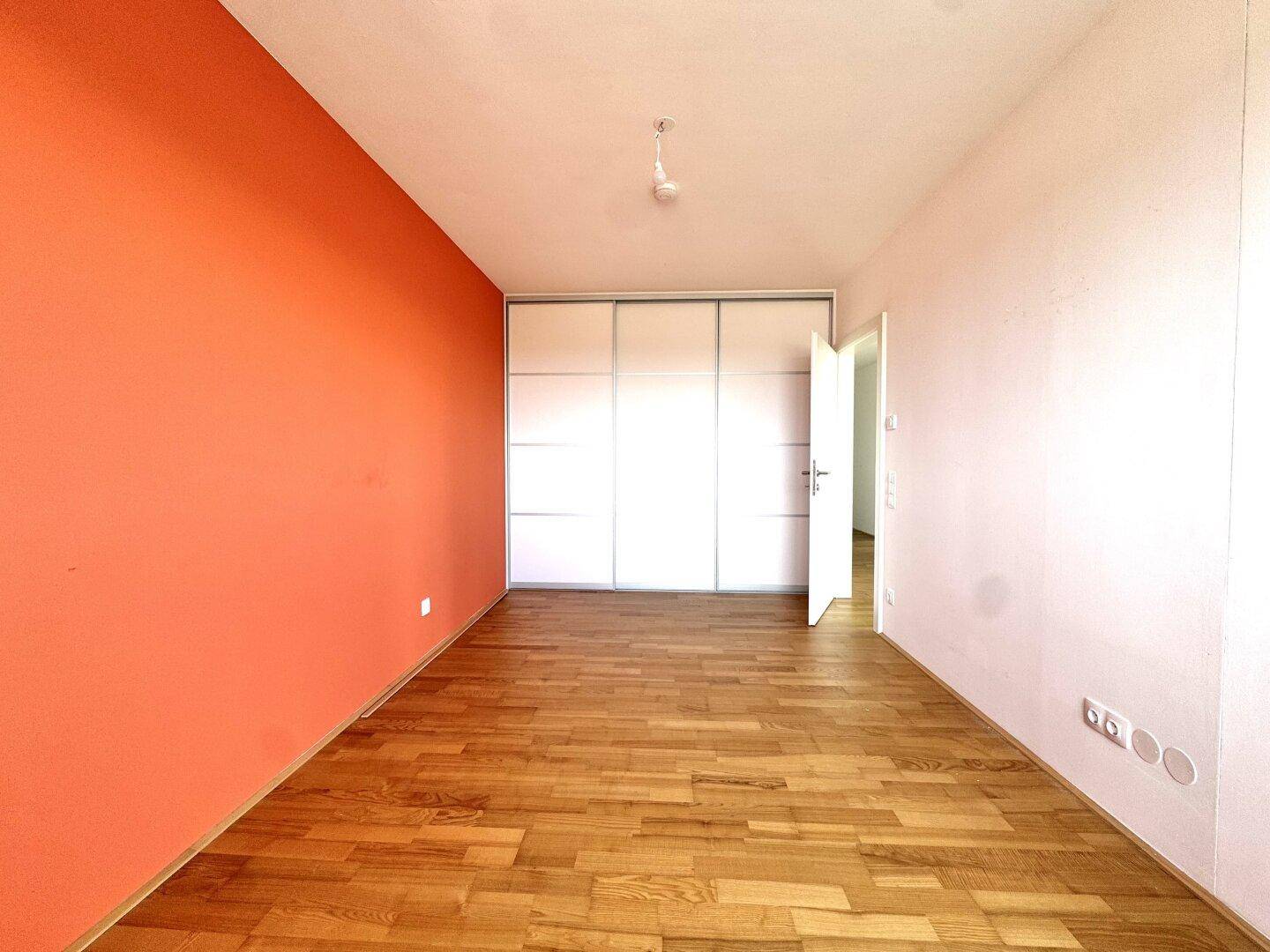 Schlafzimmer mit Parkettboden, einer farbigen Akzentwand und praktischen Einbauschränken.