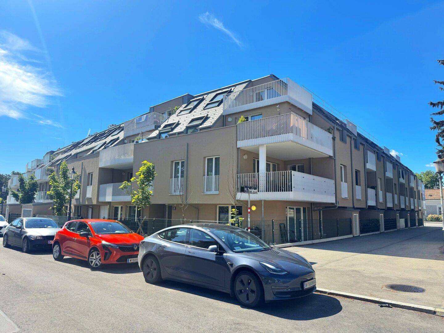 Moderne Wohnanlage mit mehreren Balkonen und großen Fenstern an einer sonnigen Straße.