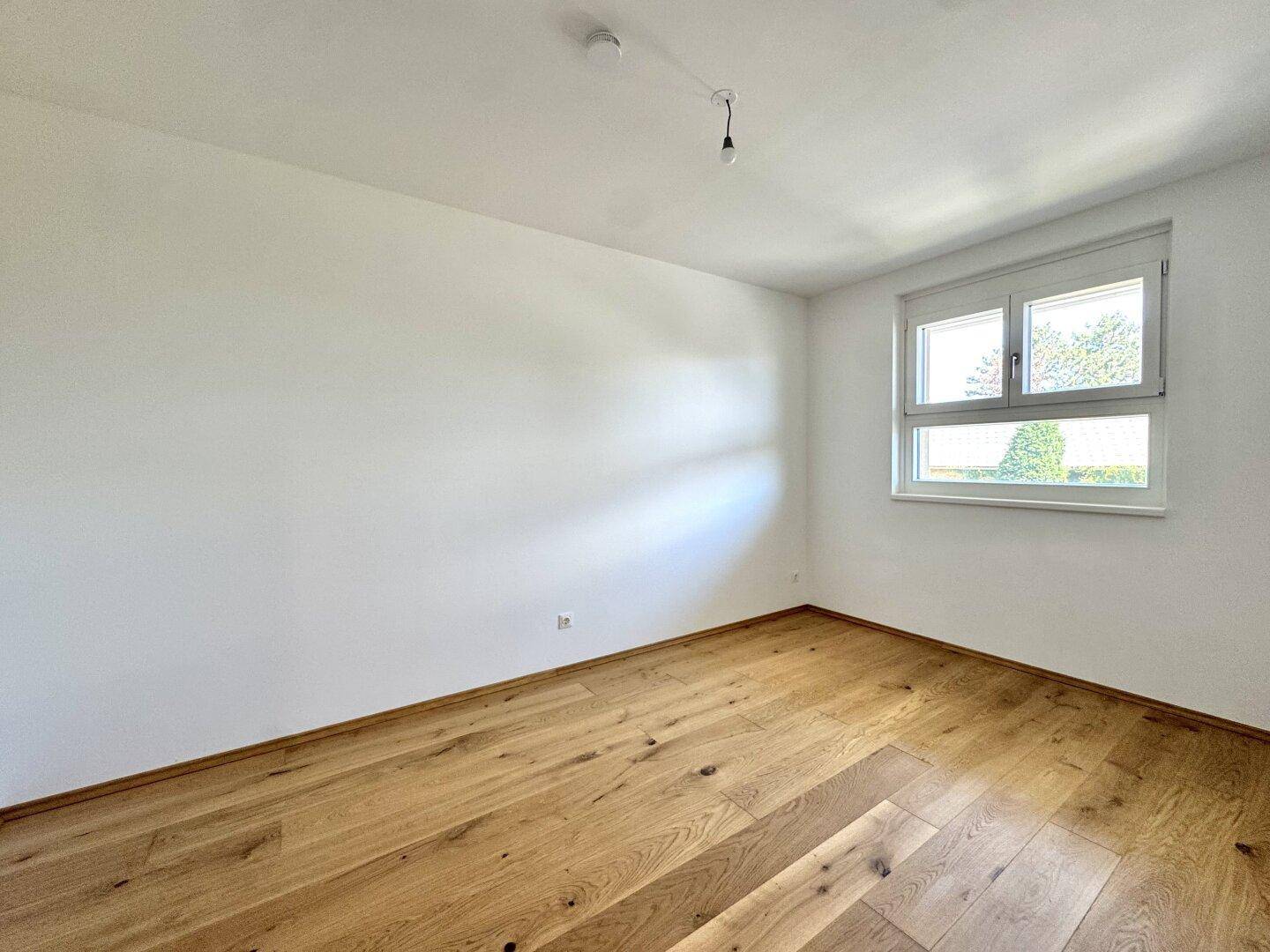 Helles, unmöbliertes Zimmer mit Parkettboden und großem Fenster.