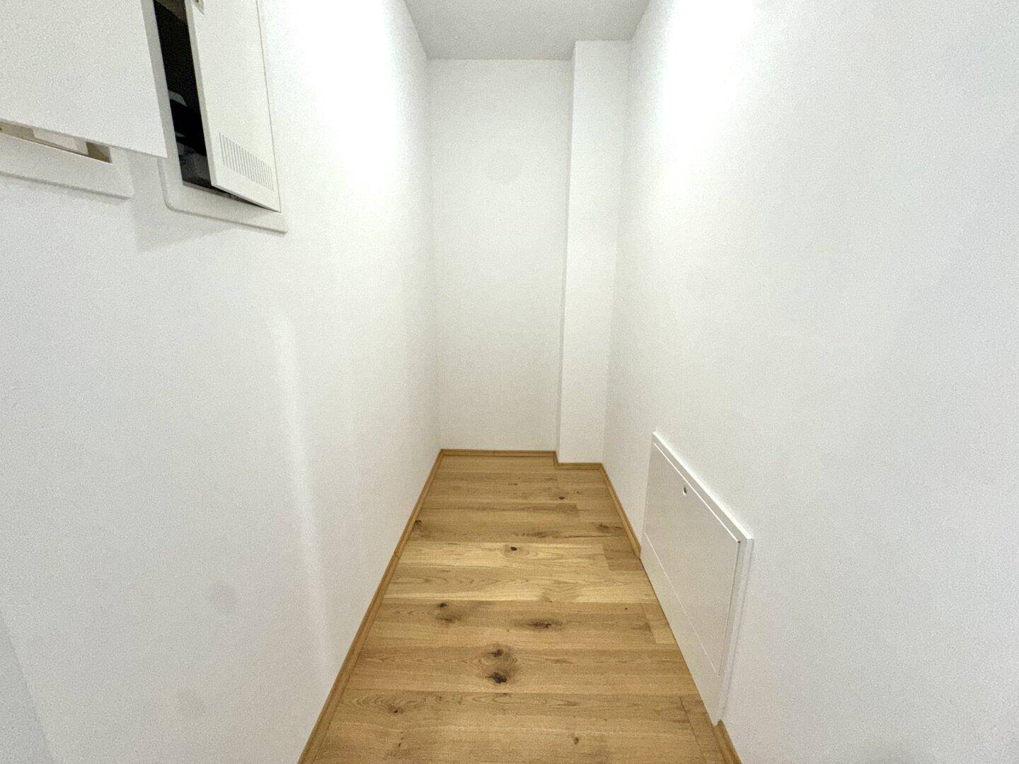 Schmaler Abstellraum mit Holzfußboden und weißen Wänden.