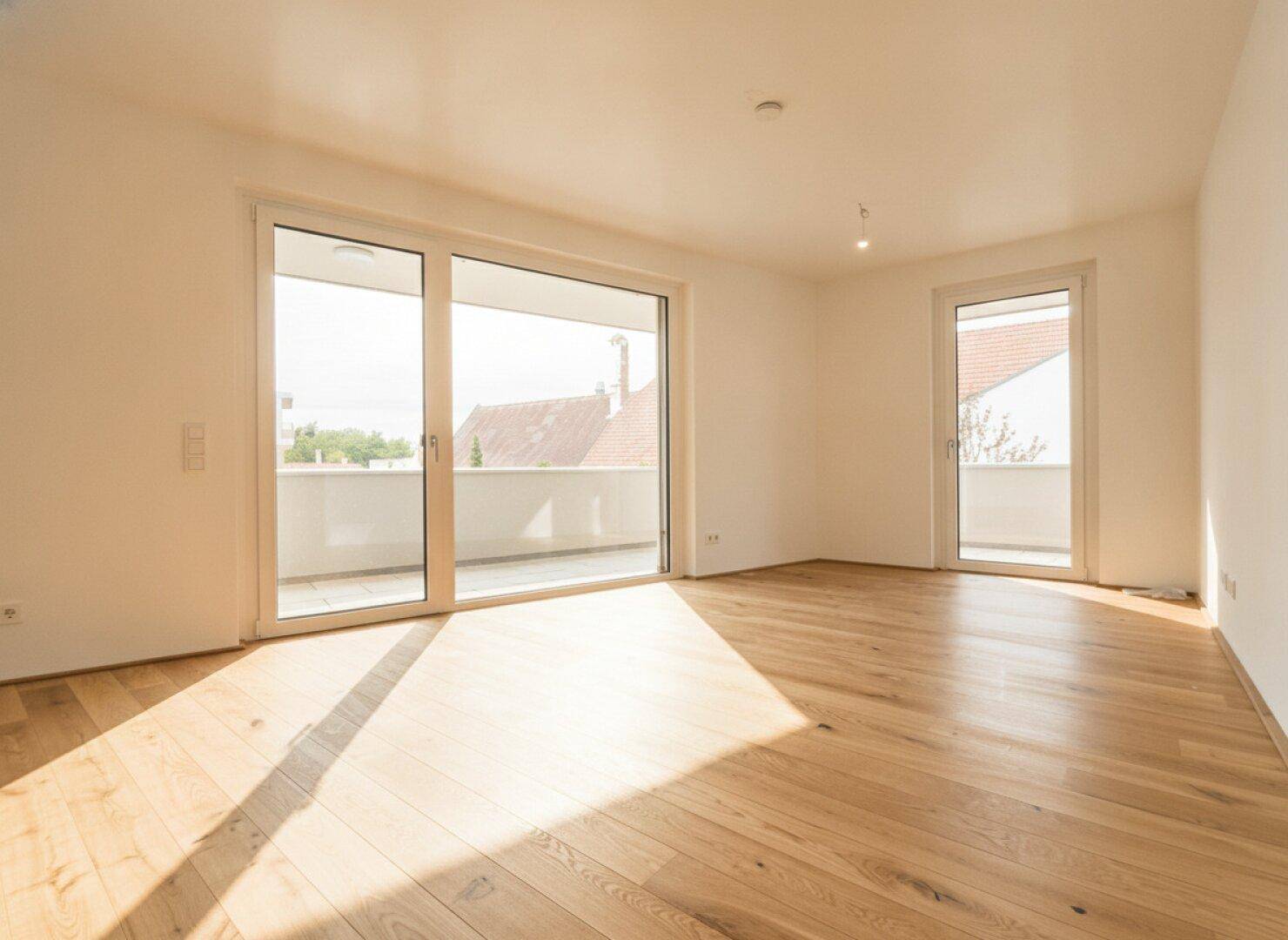 Helles, leeres Zimmer mit großen Fenstern und Zugang zu einem Balkon, ausgestattet mit Parkettboden.