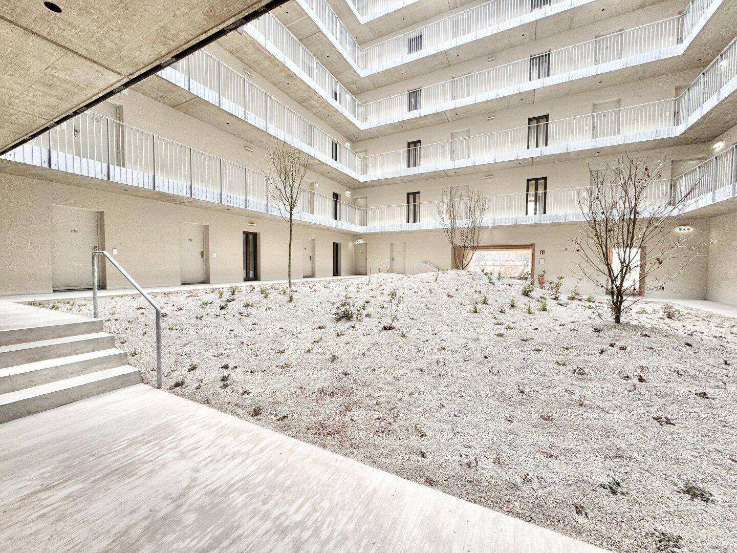Begrünter Innenhof im Erdgeschoss eines modernen Wohnkomplexes mit minimalistischer Landschaftsgestaltung.