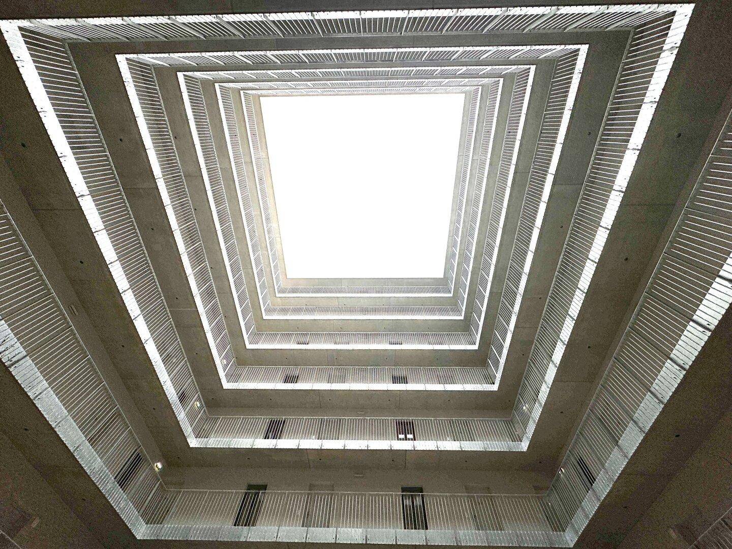 Architektonischer Innenhof mit vielen Etagen und hellem Lichteinfall von oben, der die Gänge beleuchtet.