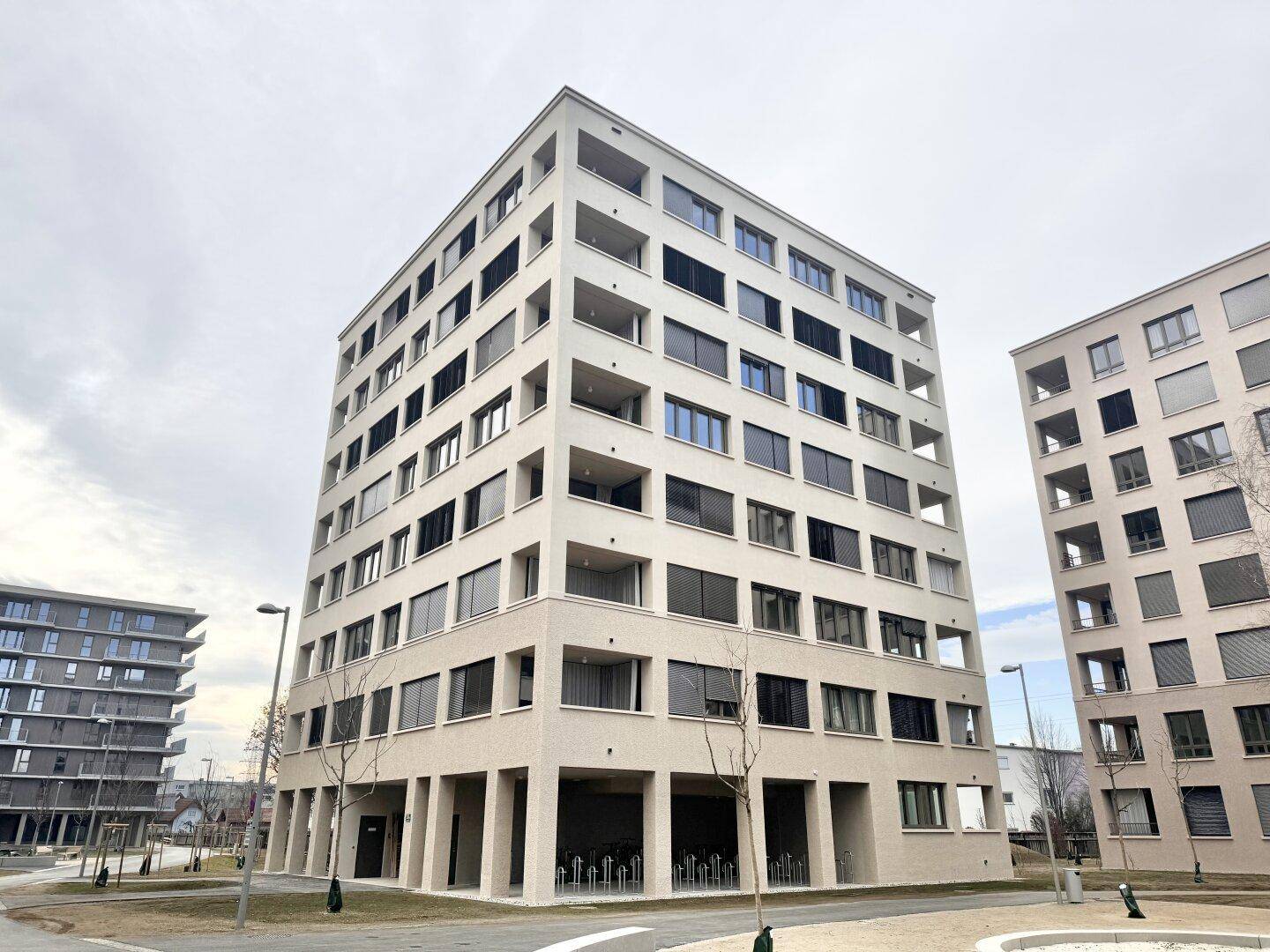 Modernes Mehrfamilienhaus mit mehreren Stockwerken und vielen Fenstern in einer städtischen Umgebung.