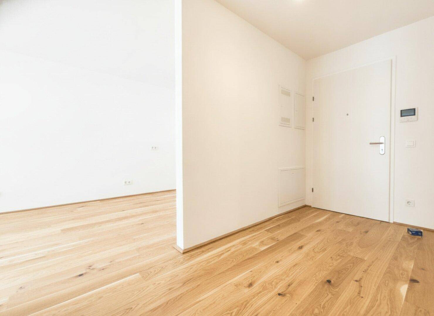 Heller Eingangsbereich mit Holzboden und weißer Wohnungstür, bietet einen freundlichen Empfang.