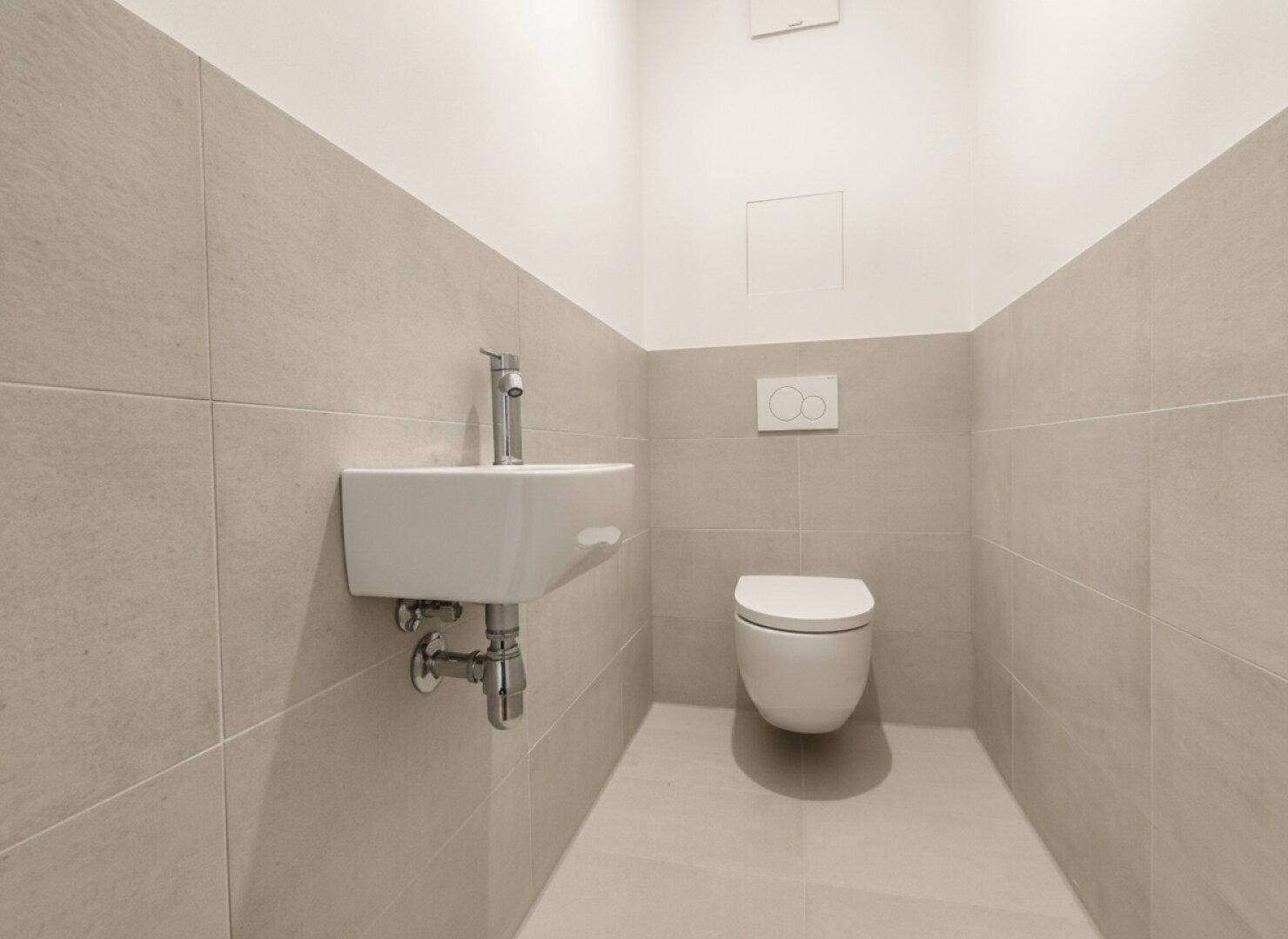 Modernes Gäste-WC mit wandhängender Toilette, kleinem Waschbecken und hellen Fliesen.