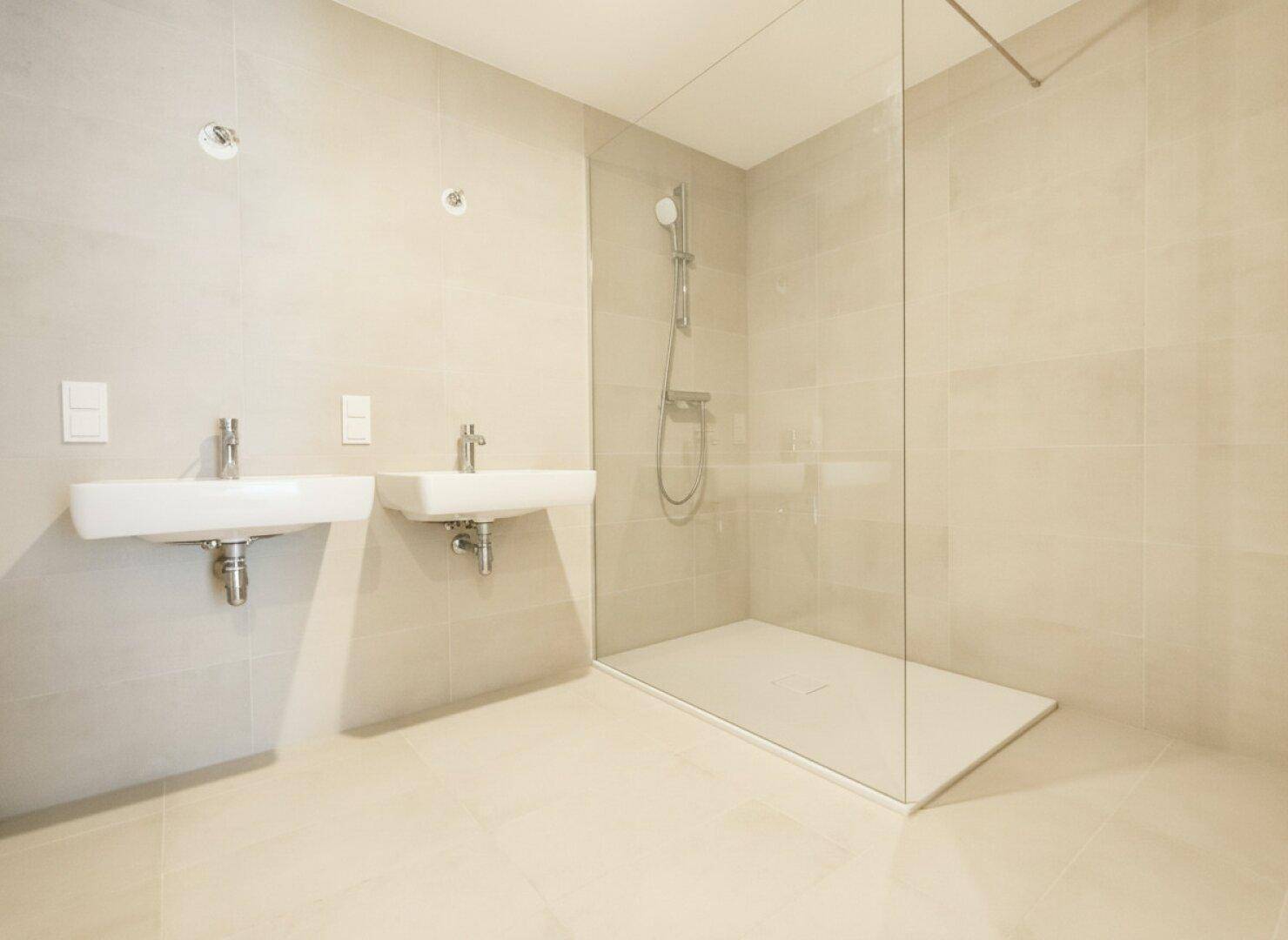 Modernes Badezimmer mit zwei Waschbecken, großer begehbarer Dusche und hellen Fliesen.