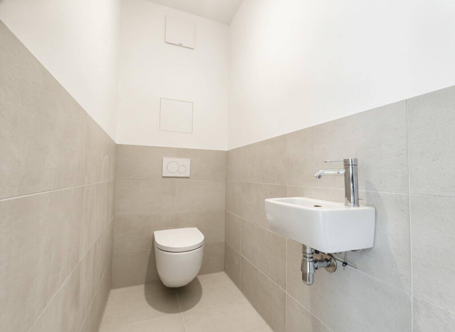 Modernes Gäste-WC mit wandhängender Toilette und kleinem Waschbecken, halbhoch gefliest.