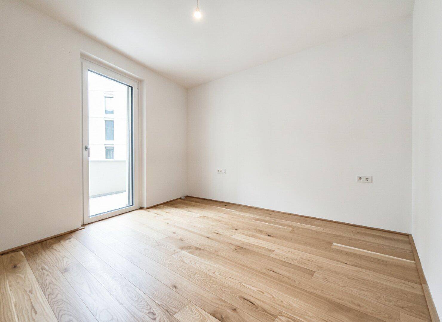 Leerer Raum mit Parkettboden und einer Tür, die zu einem Außenbereich führt, ideal für ein Schlafzimmer.