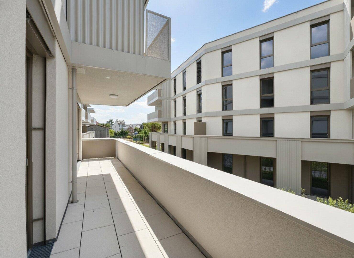 Heller Balkon mit moderner Brüstung und Aussicht auf die Wohnanlage und Grünflächen.