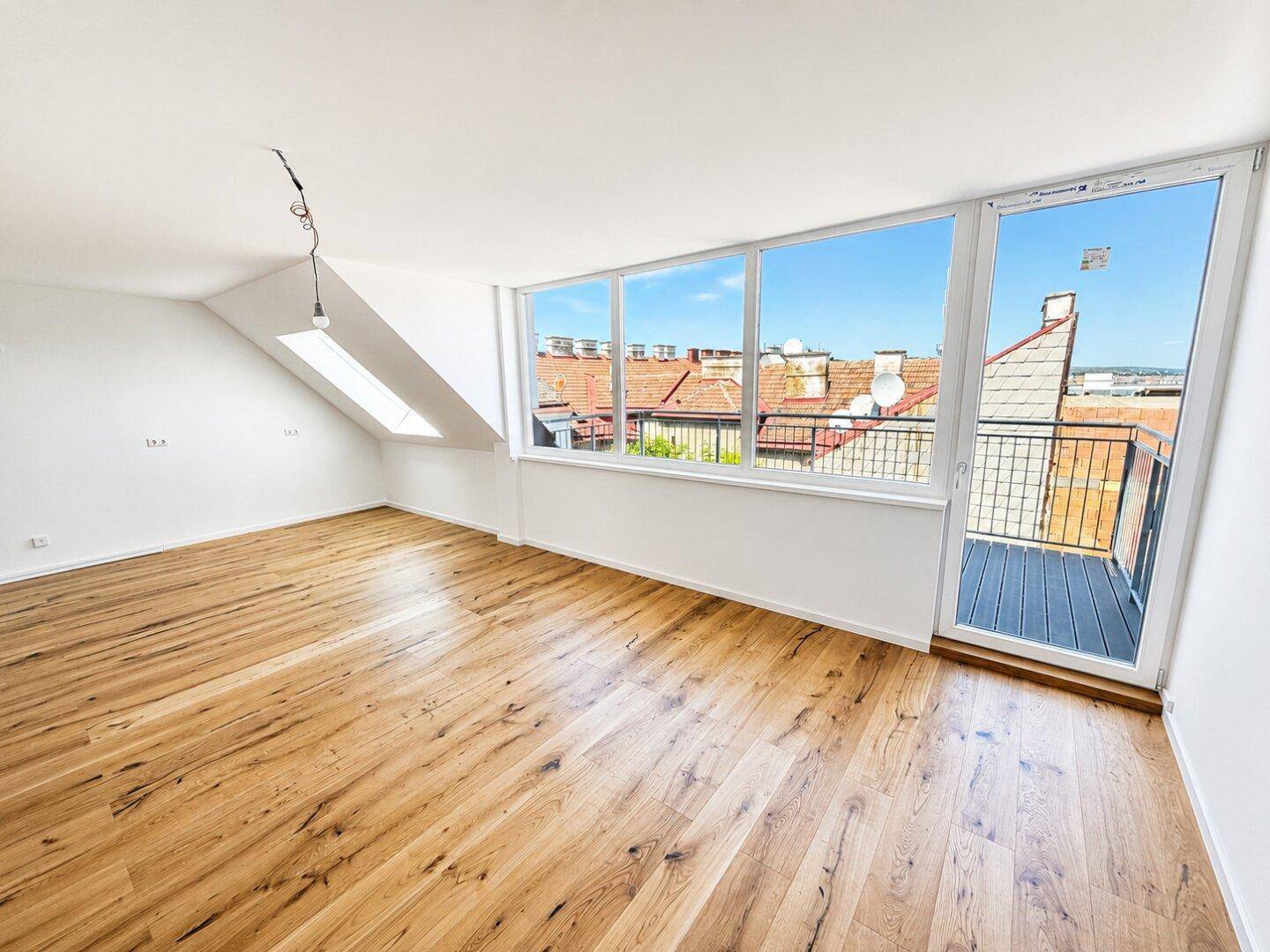 Lichtdurchfluteter Wohnraum mit Holzboden, Dachschrägen und Zugang zum Balkon.