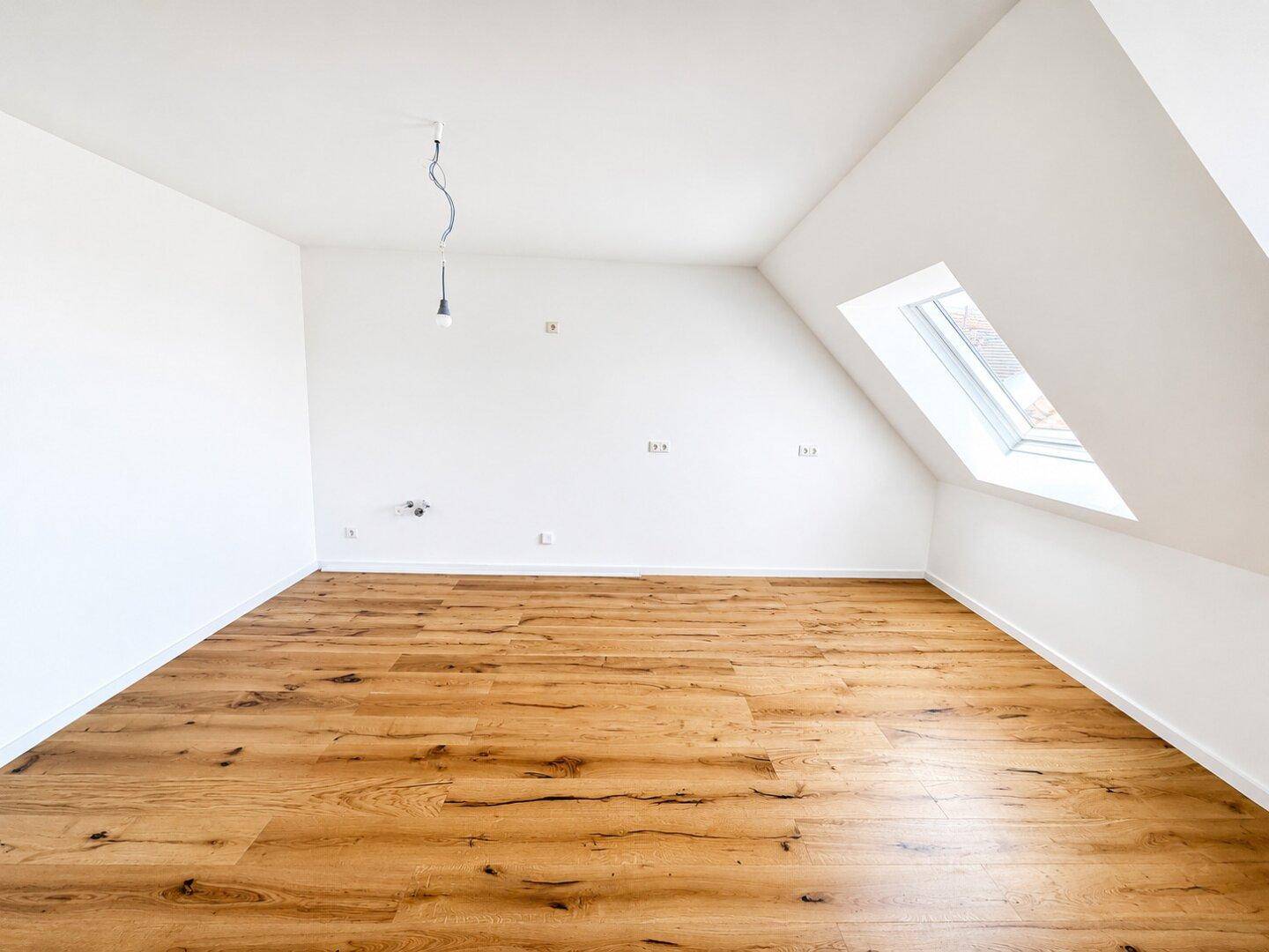 Helles Zimmer mit Holzboden, Dachschräge und einem großen Dachfenster für viel Tageslicht.