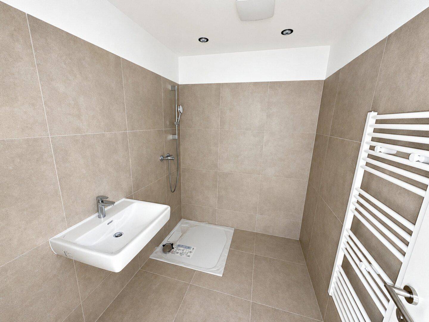 Modernes Badezimmer mit beigefarbenen Fliesen, wandhängendem Waschbecken und ebenerdiger Dusche.