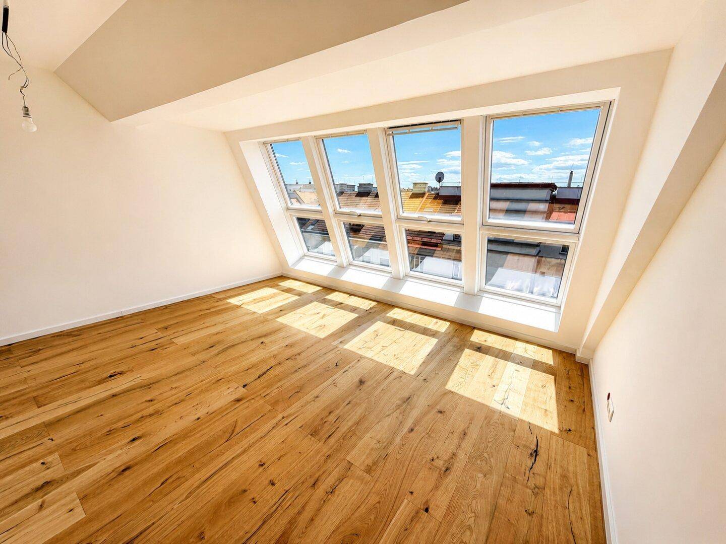 Heller Wohnraum mit Holzboden, Dachschrägen und einer großen Fensterfront für viel Tageslicht.