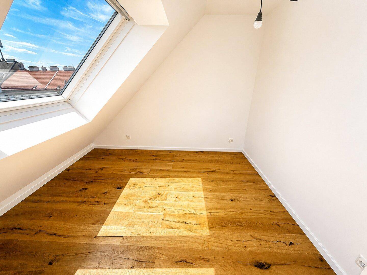 Helles Zimmer mit Holzboden, Dachschräge und einem großen Dachfenster, das den Raum mit Licht füllt.