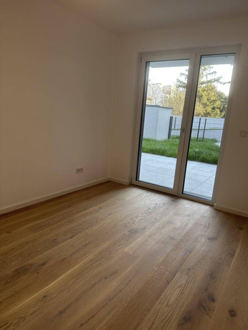 Helles Zimmer mit Holzdielenboden und großem Zugang zu einer gefliesten Terrasse und dem Gartenbereich.
