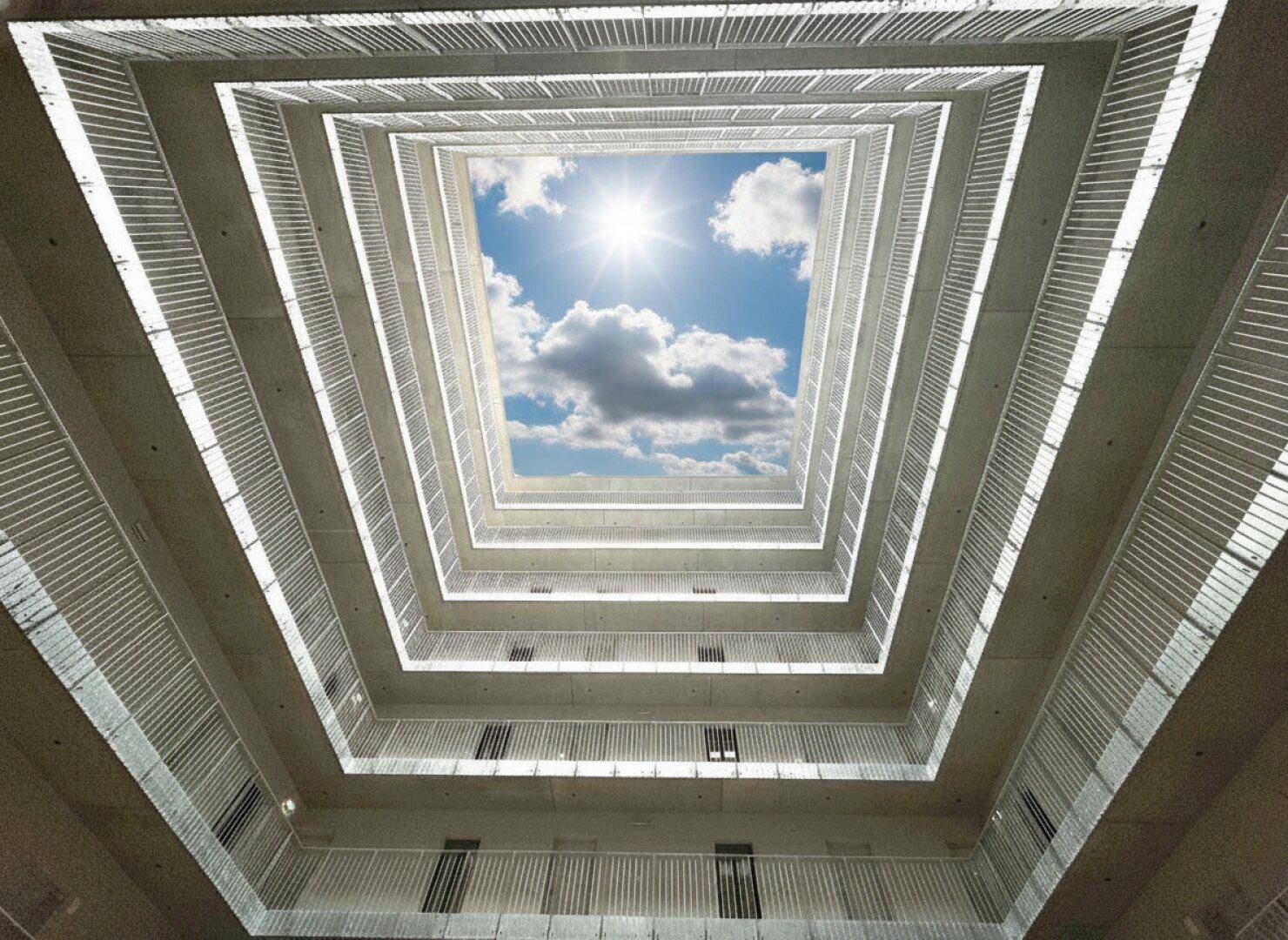 Zentraler Innenhof eines modernen Gebäudes mit Blick auf den blauen Himmel und die Sonne.