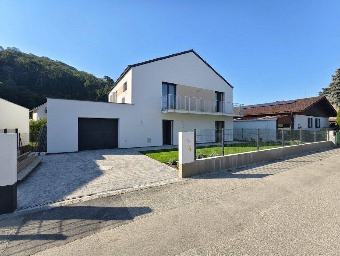 Vorderansicht des modernen Hauses mit integrierter Garage, gepflasterter Einfahrt und kleinem Vorgarten.