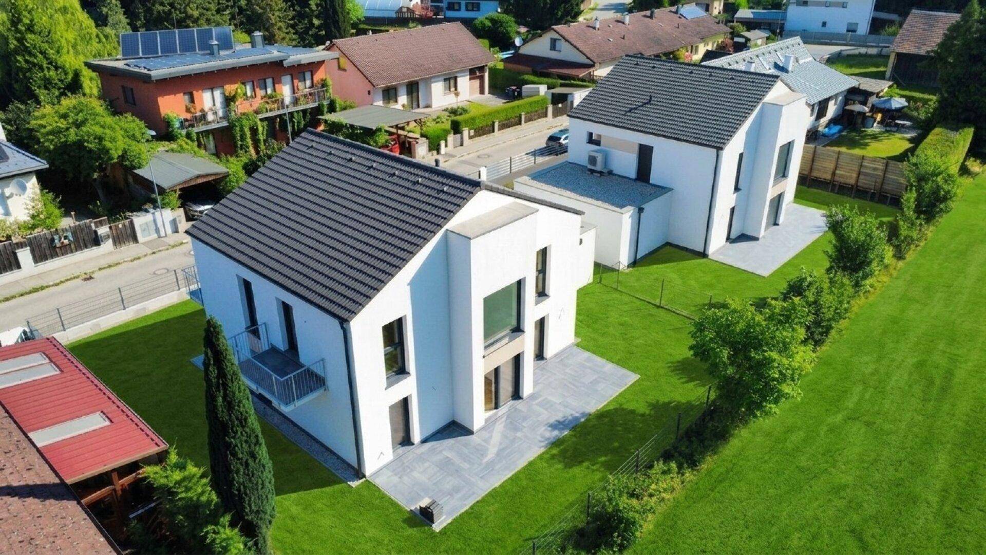 Zwei moderne Einfamilienhäuser mit großzügigen Gärten und Terrassenbereichen.