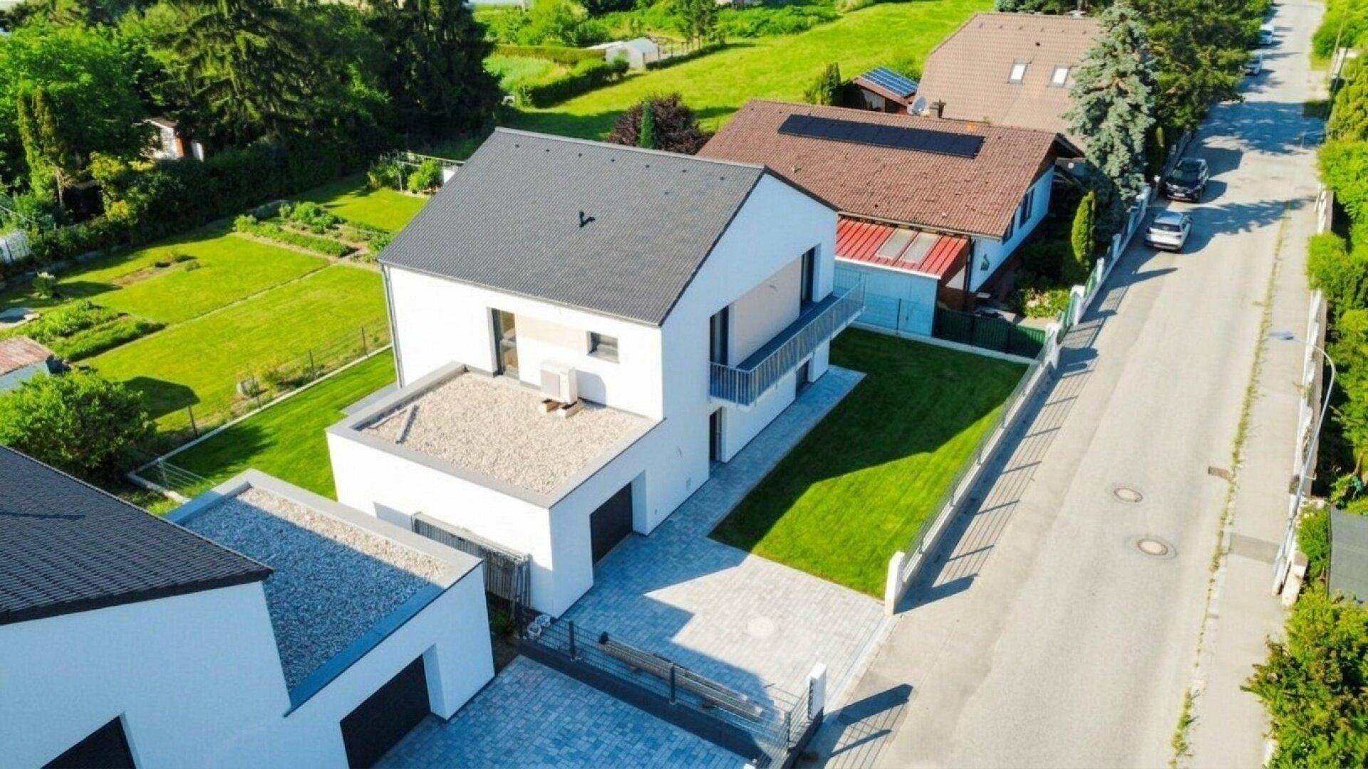 Neubau-Einfamilienhaus mit moderner Fassade, Balkon und gepflasterter Einfahrt.