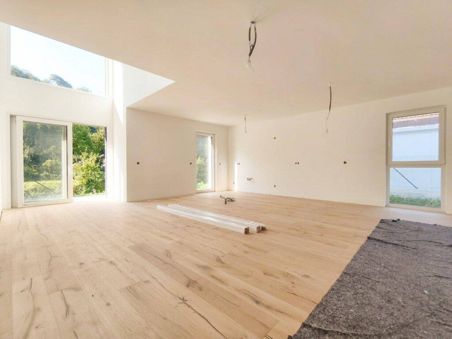 Heller, unmöblierter Wohnbereich mit großen Fenstern, Holzboden und Zugang zum Garten.