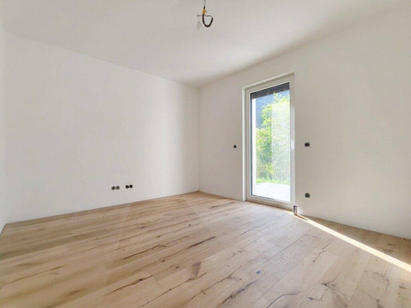 Helles Schlafzimmer mit Holzboden und großem Fenster, das viel Tageslicht hereinlässt.