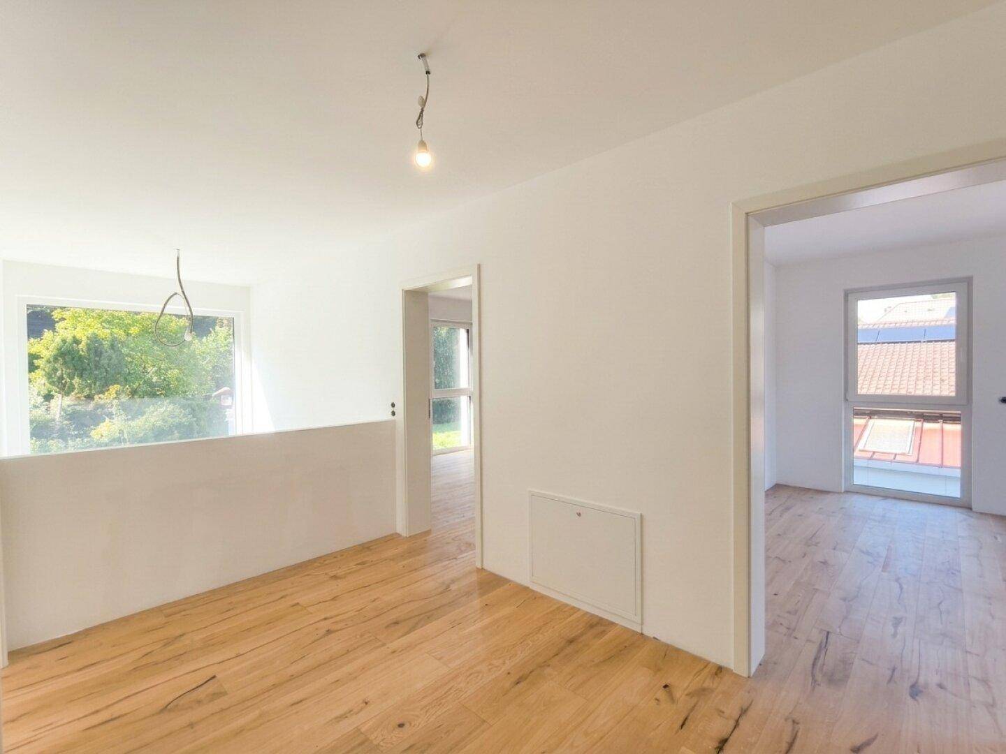 Heller Flur im Obergeschoss mit Holzboden und Zugang zu weiteren Zimmern.