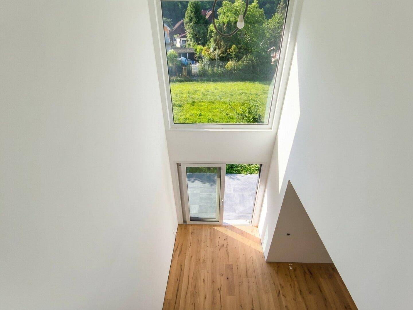 Blick vom Obergeschoss in den unteren Bereich mit großen Fenstern und viel Tageslicht.