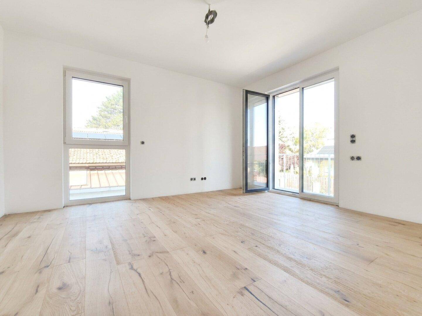 Geräumiges Schlafzimmer mit Holzboden, großen Fenstern und direktem Zugang zum Balkon.