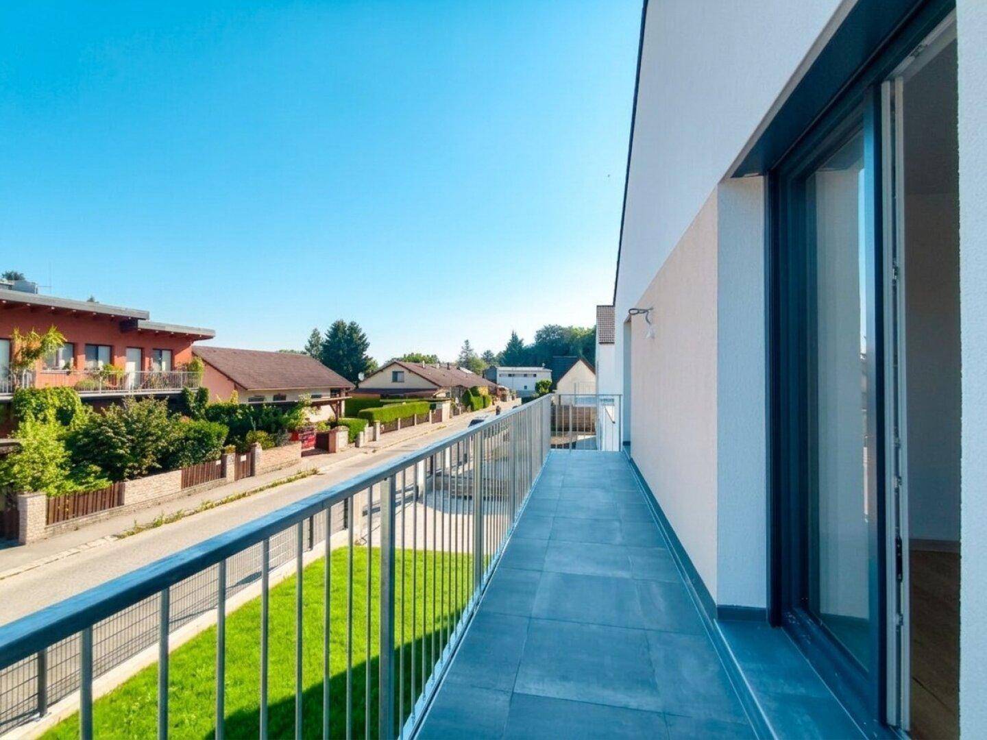 Langer Balkon mit Metallgeländer und Blick auf die Straße und die umliegende Wohngegend.