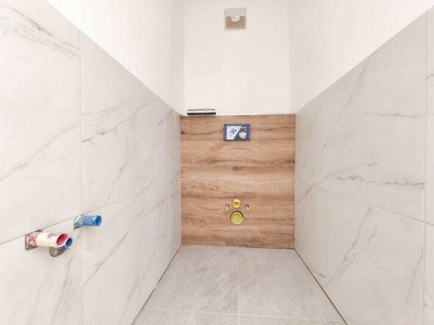 Gäste-WC im Bau mit modernen Fliesen in Marmoroptik und Holzakzenten, bereit für die Installation.