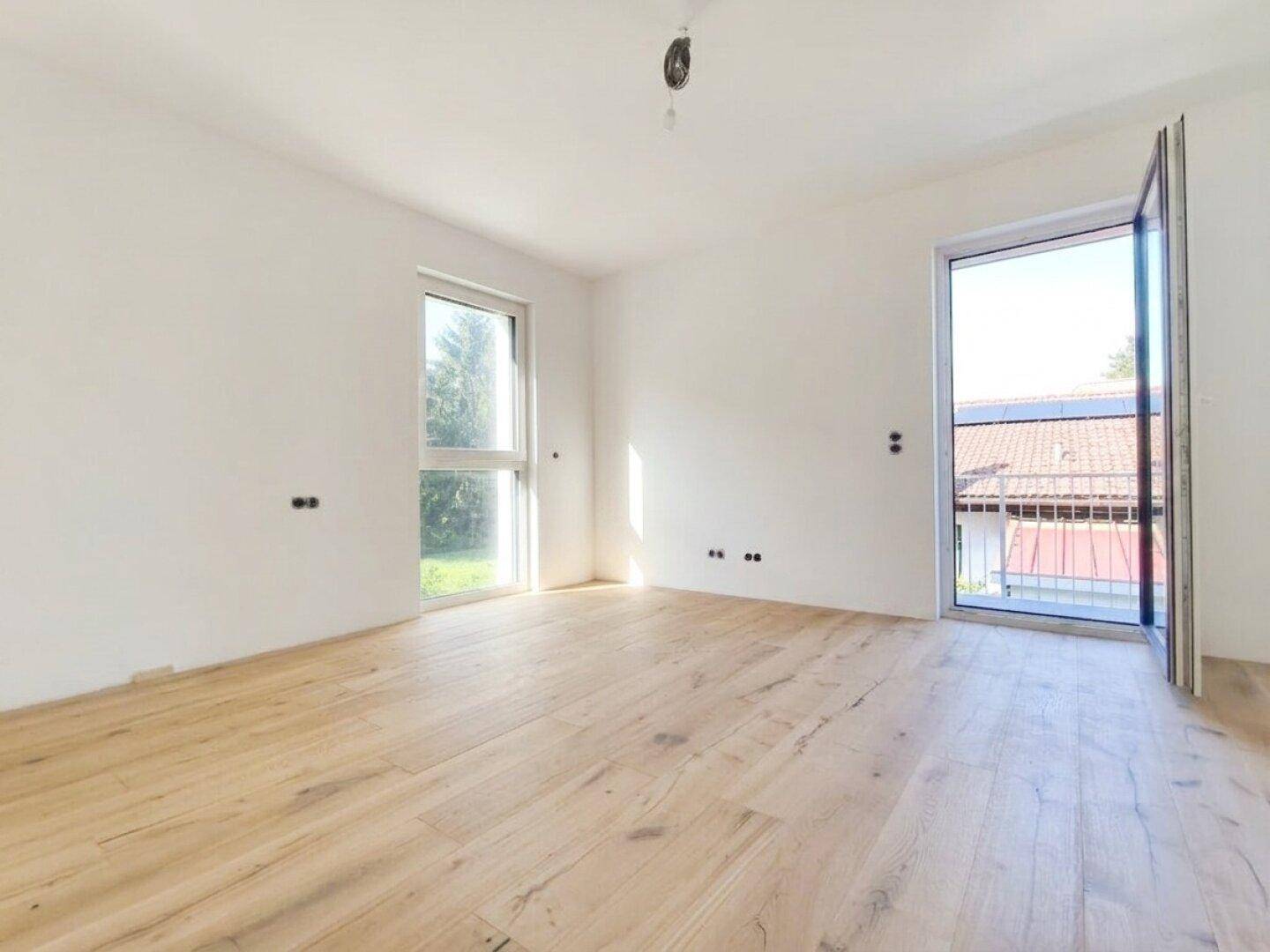 Geräumiges Schlafzimmer mit Holzboden und zwei großen Fenstern, die eine helle Atmosphäre schaffen.