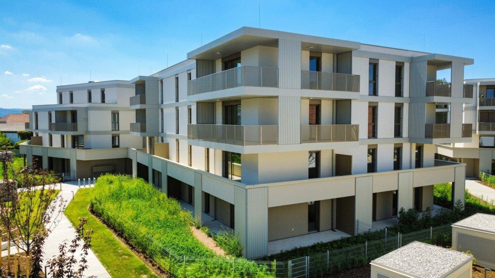 Ansicht der modernen Wohngebäude mit hellen Fassaden und zahlreichen Balkonen in grüner Umgebung.