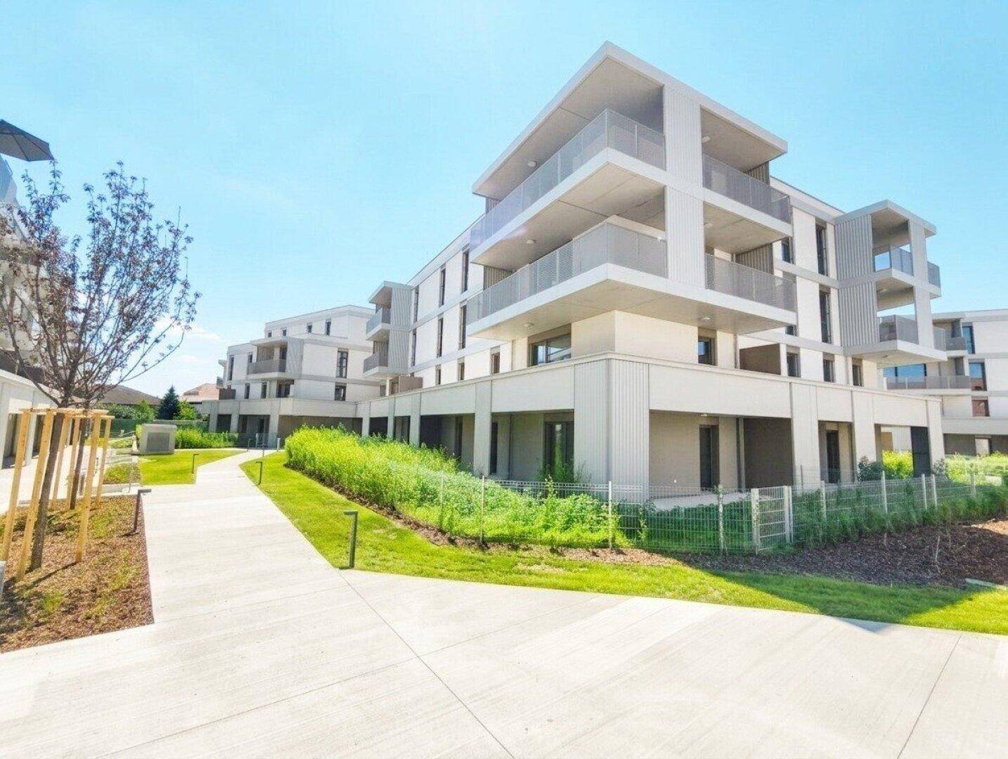 Blick auf die moderne Fassade des Apartmentgebäudes mit gepflegten Gehwegen und Grünflächen.