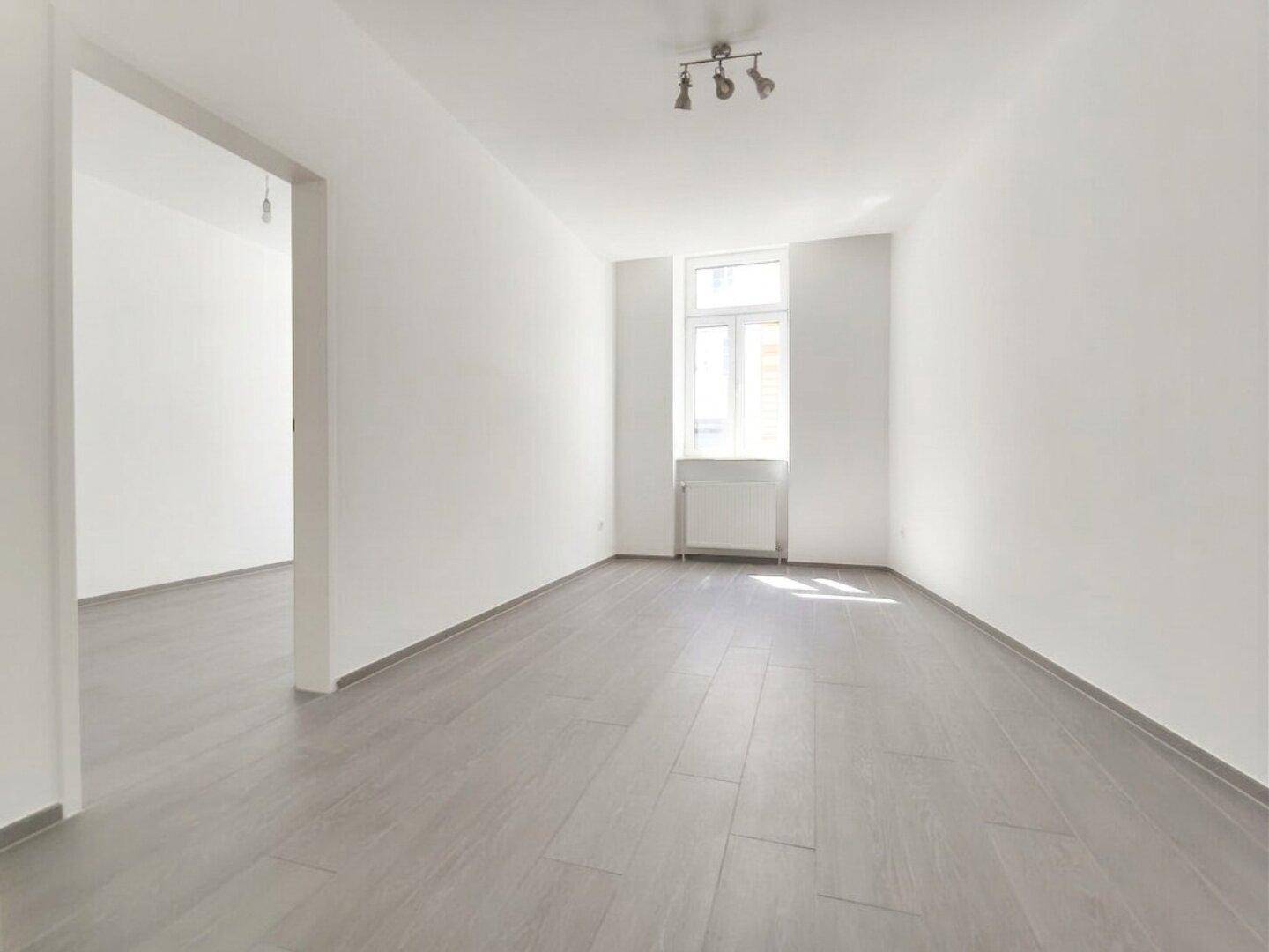 Heller, leerer Raum mit modernem grauen Laminatboden und großem Fenster.