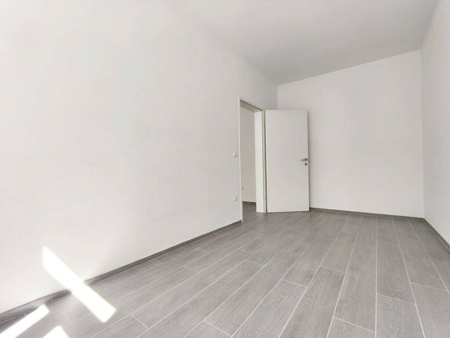 Heller, leerer Raum mit grauem Laminatboden und weißer Tür, bereit zum Einrichten.