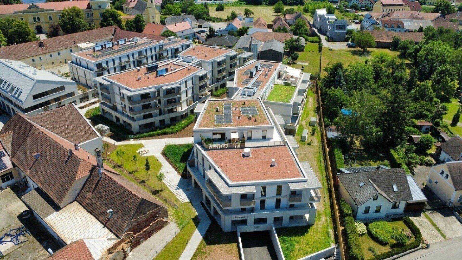 Luftaufnahme der Wohnsiedlung mit modernen Gebäuden, umgeben von Grünflächen und älteren Häusern.