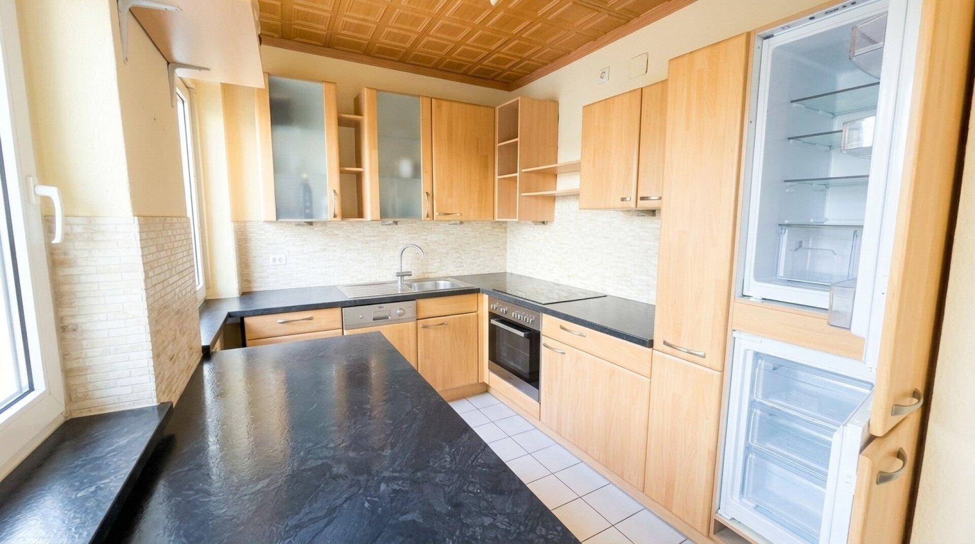 Funktionale Küche mit hellen Holzschränken, dunkler Arbeitsplatte und integriertem Kühlschrank.