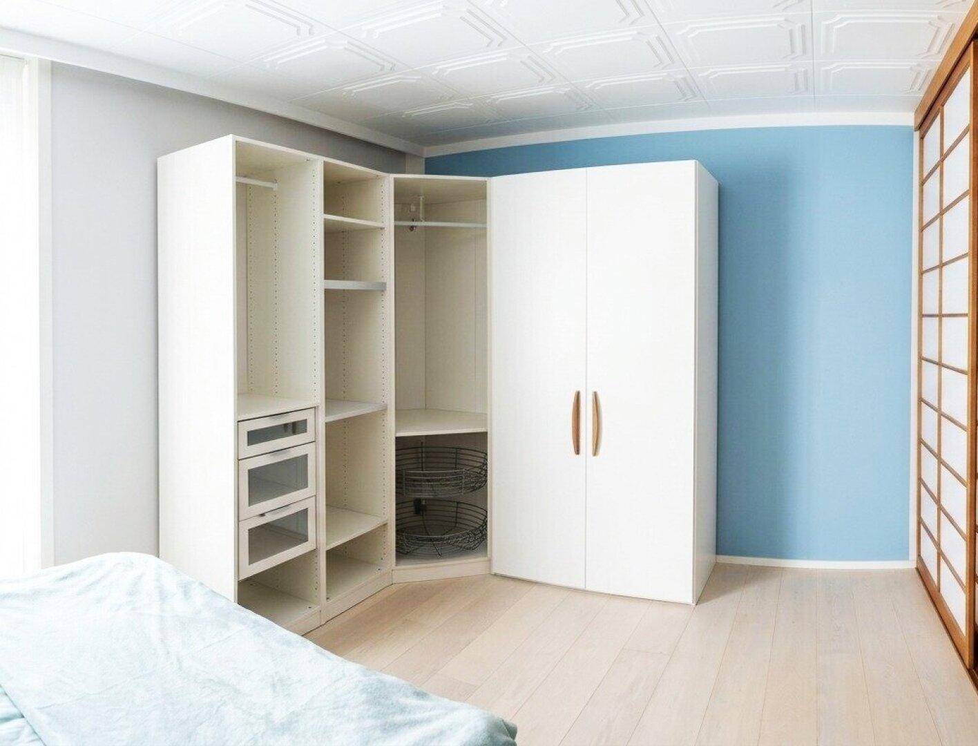 Schlafzimmer mit weißem Eckkleiderschrank, hellem Holzboden und blauer Akzentwand.