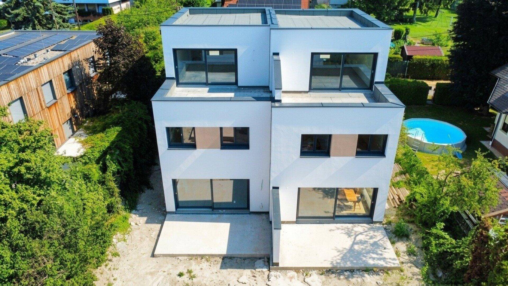Ansicht eines modernen Doppelhauses mit weißer Fassade und großen Fensterfronten, umgeben von Natur.