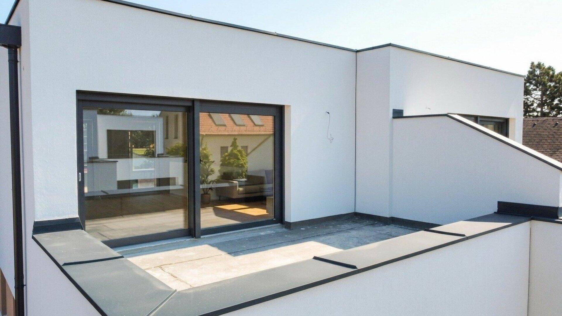 Unmöblierte Dachterrasse mit Schiebefenstern und Blick auf die Nachbarschaft und grüne Umgebung.