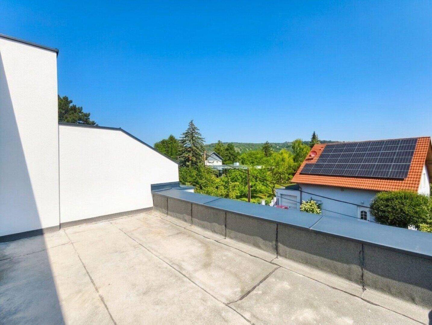 Unmöblierte Dachterrasse mit weitem Blick über die grüne Umgebung und benachbarte Dächer.